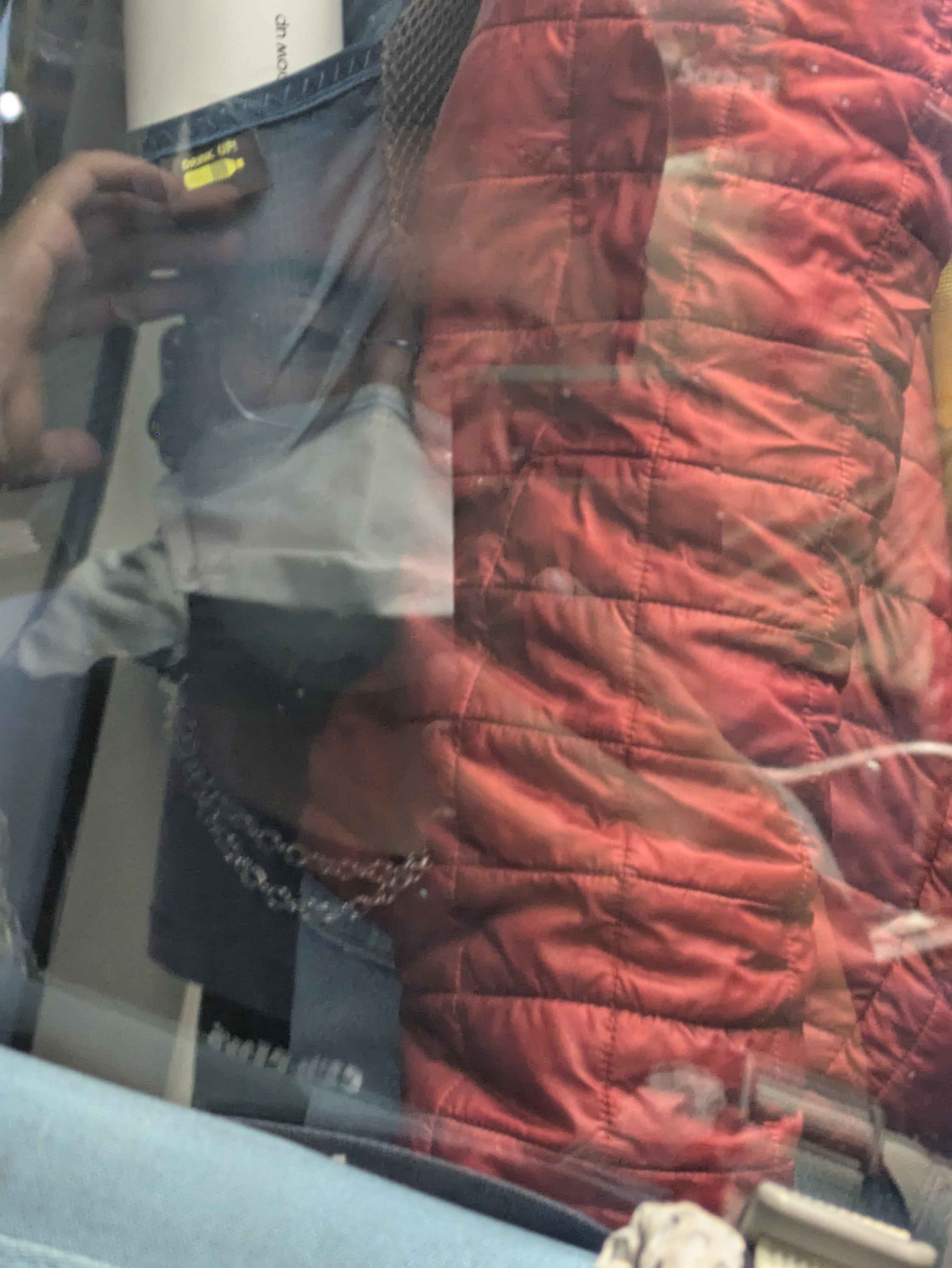 Walden, a brown man in a duckbill respirator, is pictured in the reflection on a pane of glass.