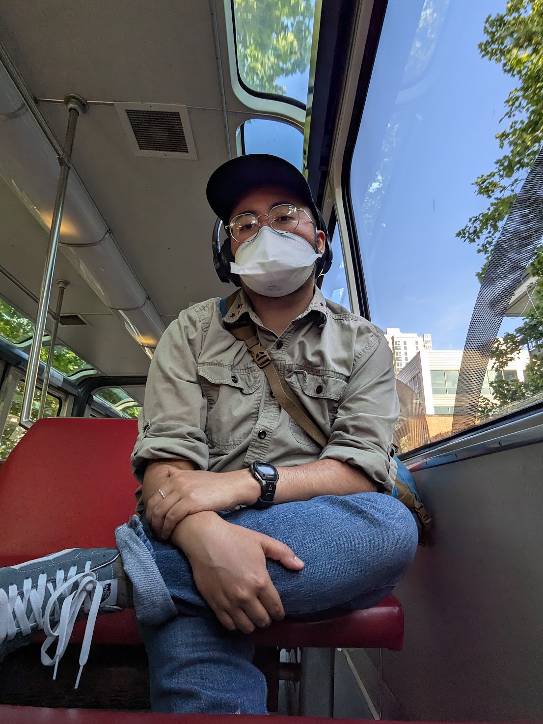 Walden, a brown man in a duckbill respirator, sits with one knee crossed over the other.